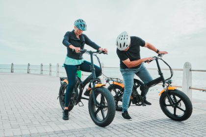 Mature couple, electrical or checking bike by beach in bonding transportation, clean energy or sust