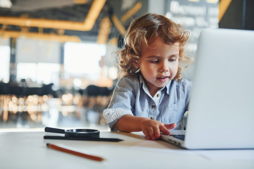 Smart child in casual clothes using laptop for education purposes or fun