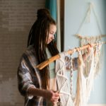 Young woman with dreadlocks weaves home decor from cotton thread macrame.