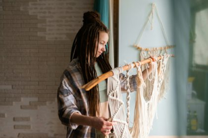 Young woman with dreadlocks weaves home decor from cotton thread macrame.